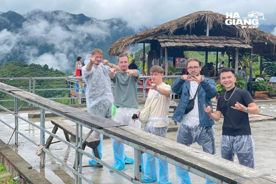Traveler wearing packable rain jacket and rain pants on misty Ha Giang mountain road with jeep in background