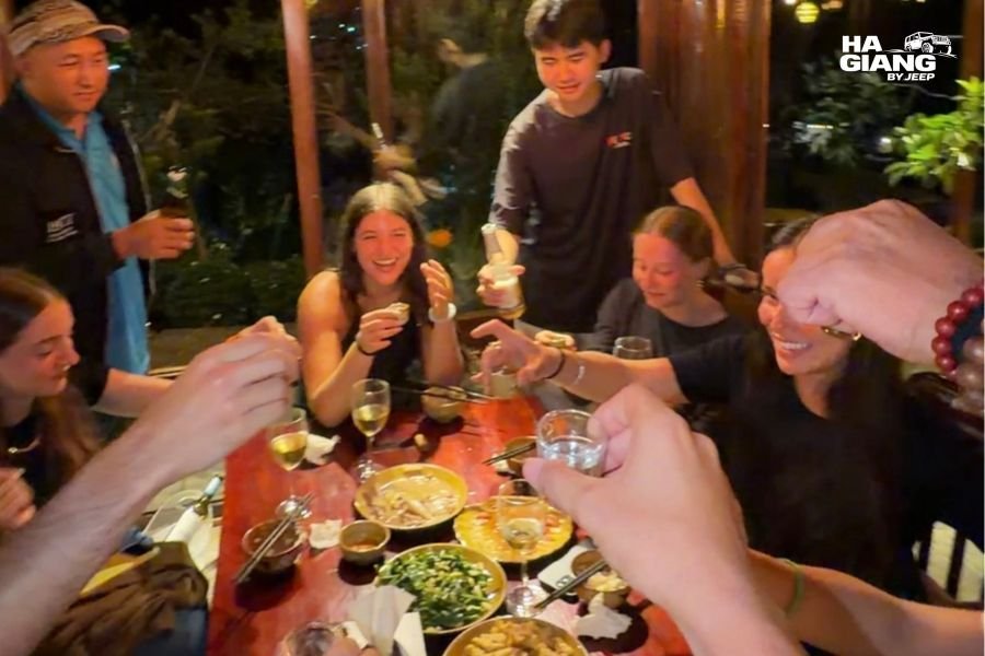 Travelers and homestay family sharing traditional meal together around table